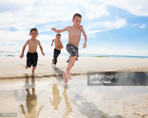 three boys jumping over a puddle - anna maria island stock-fotos und bilder