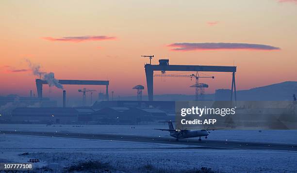 Flybe aircraft takes off from the Belfast City Airport in Belfast, Northern Ireland, on December 23, 2010 as the famous Harland and Wolff cranes are...