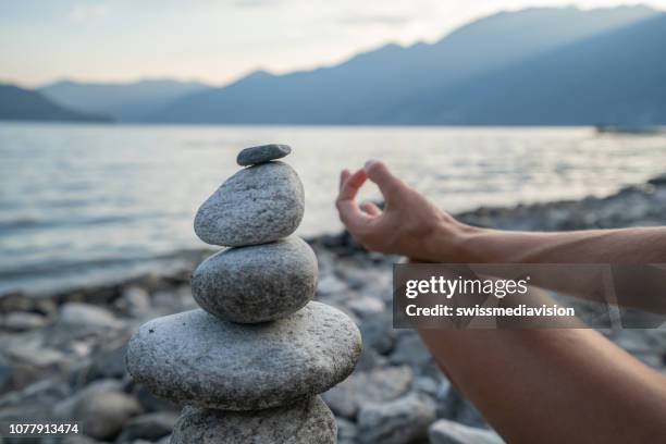 detail der person, die ausübung von yoga und meditation in der nähe von stack rock am see bei sonnenuntergang - stone hand stock-fotos und bilder