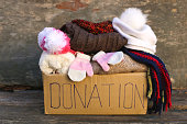 Donation box with warm winter clothes on old wooden background.
