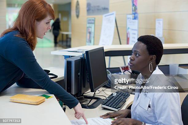 upset patient explaining problem to medical receptionist - angry customer photos et images de collection