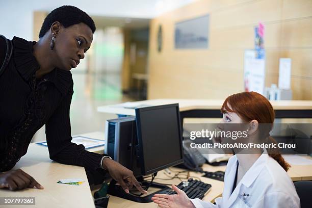 female patient explaining problem to medical receptionist - switchboard stock pictures, royalty-free photos & images