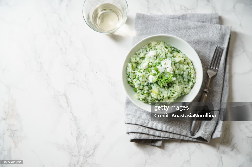 Spinach risotto with a glass of white wine on marble background with copy space
