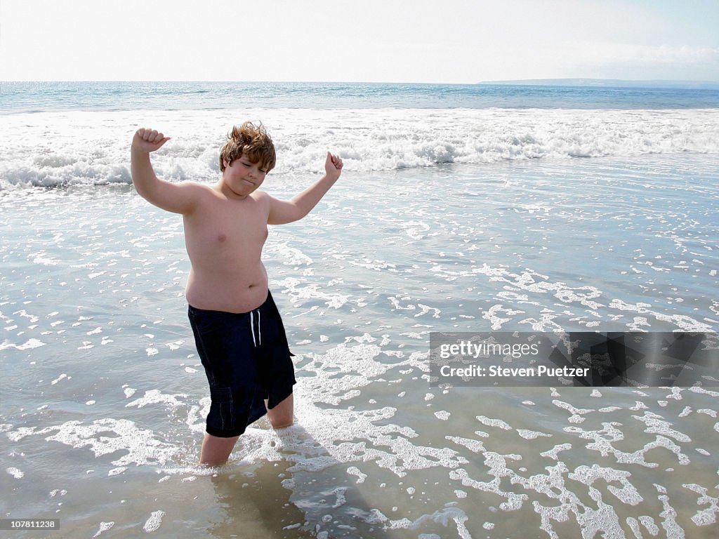 Overweight boy dancing in water at the beach