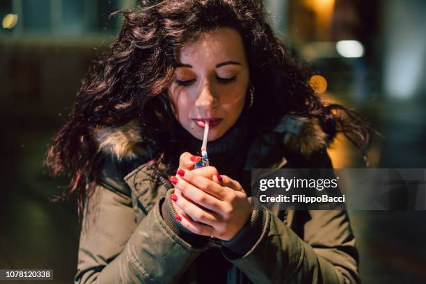 jeune femme adulte éclairage cigarette dans la ville pendant la nuit - femme et fumeuse photos et images de collection