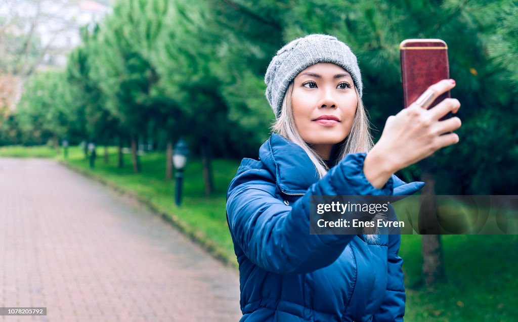 Mujer tomando selfie por la cámara de su teléfono móvil en parque público