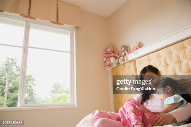 asian mother and daughter sitting in bed at home - contemplation family stock pictures, royalty-free photos & images