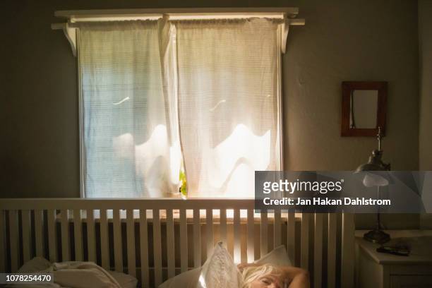 woman asleep in bed in front of window with curtain and geranium - eine seniorin allein stock-fotos und bilder