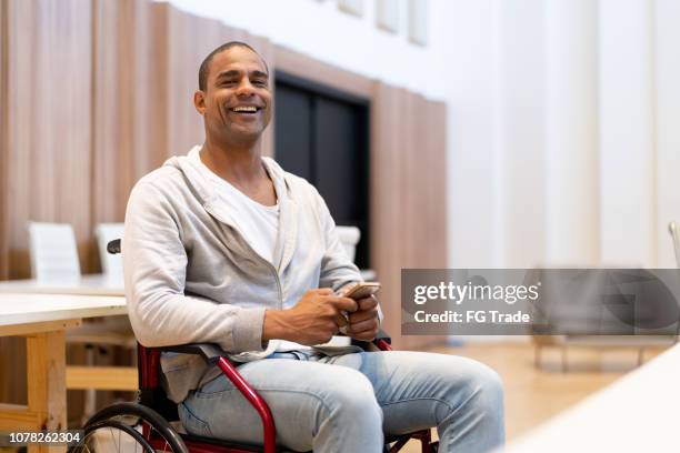 disabled man sitting in a wheelchair using mobile at workplace - man in wheelchair stock pictures, royalty-free photos & images