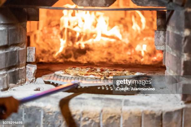 pizza op een houtvuur bakstenen oven wordt gebakken - haardvuur stockfoto's en -beelden