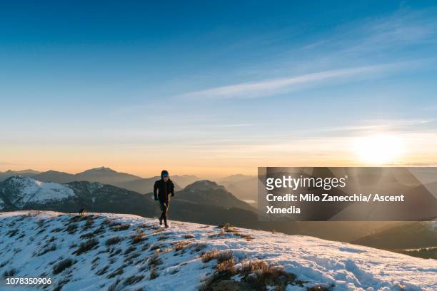 trail runner traverses high alpine ridge, above valley - winter sport stock-fotos und bilder