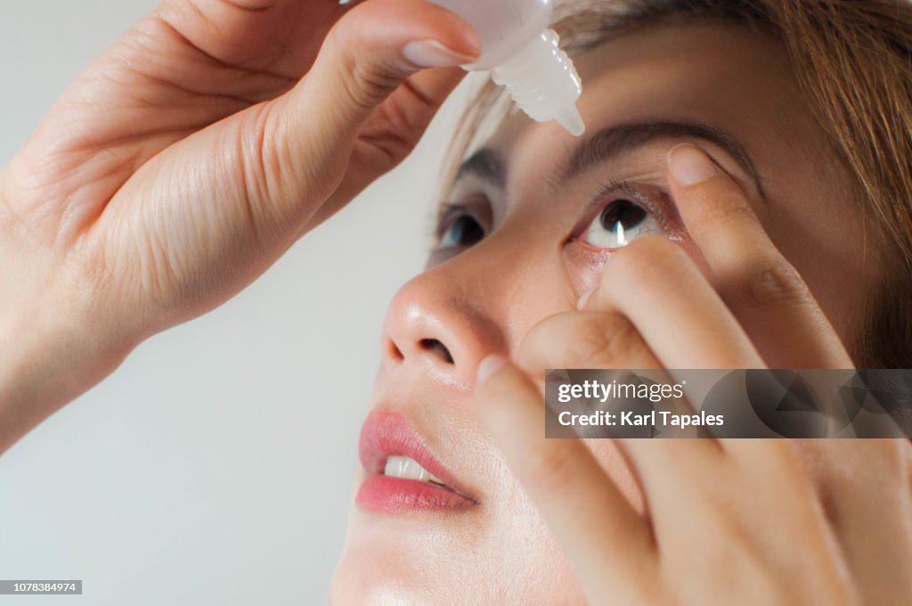 A young woman is applying medicine drops on her eyes