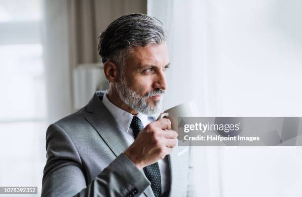 a portrait of a mature attractive businessman standing in an office, holding coffee. - coffee moustache stock pictures, royalty-free photos & images