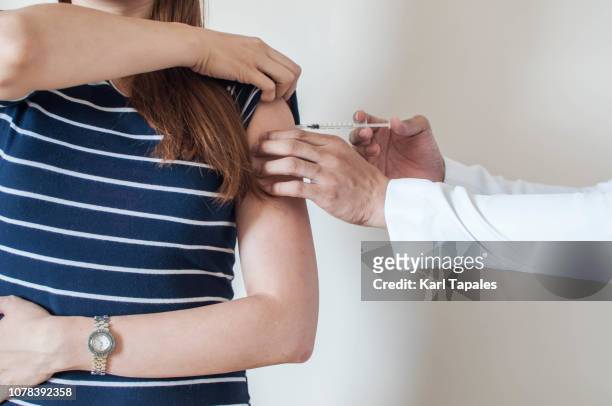 a doctor is giving a vaccine to a young woman - arm needle stockfoto's en -beelden
