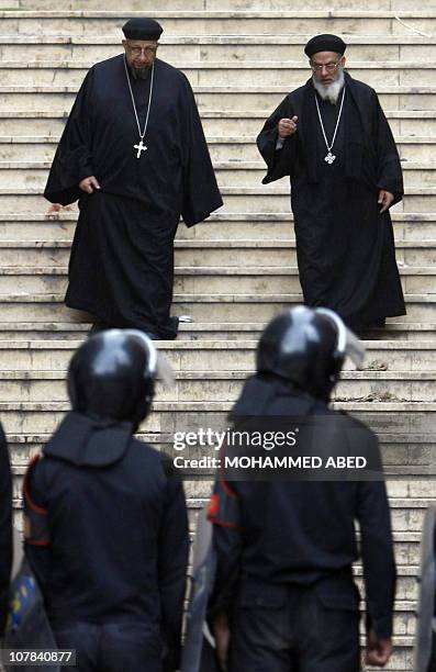 Egyptian riot police stand guard as coptic priests walk down steps outside the Al-Qiddissine church following an overnight car bomb attack on the...