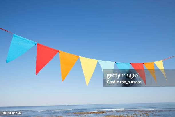 colorful bunting flags/ pennant chain for party decoration by the sea against sky - banderin fotografías e imágenes de stock