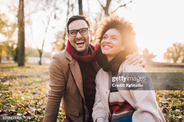 smiling couple sitting in the park - autumn friends coats stock pictures, royalty-free photos & images