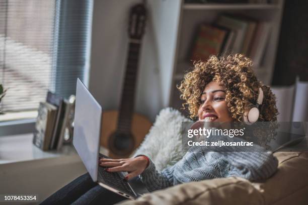 young girl with laptop sitting in  living room - headphone girls stock pictures, royalty-free photos & images