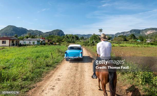 coche clásico pasa a un hombre a caballo en viñales, cuba - viñales cuba fotografías e imágenes de stock