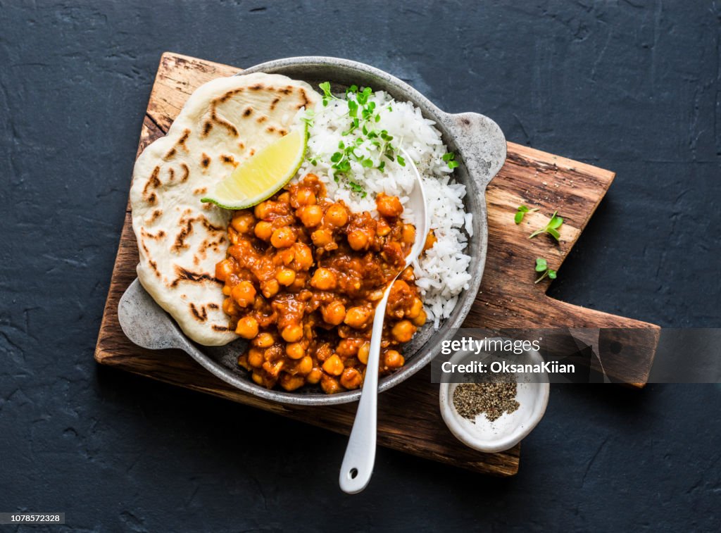 Indian spicy chickpeas curry with rice and naan bread in pan on dark background, top view. Healthy tasty vegetarian food