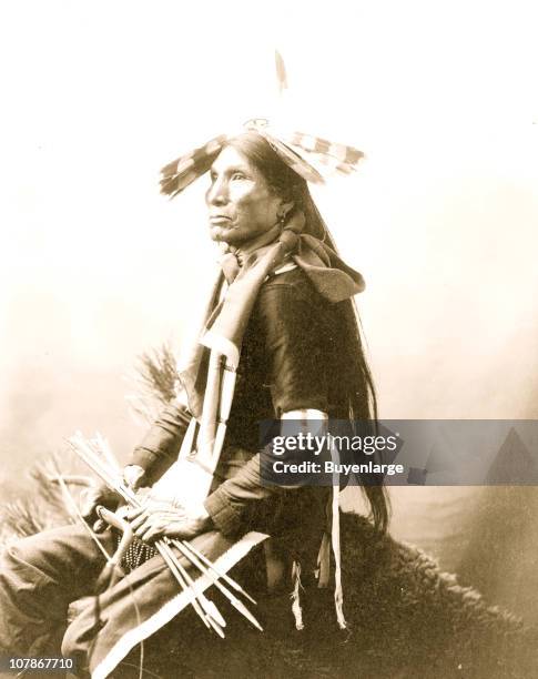 Good Eagle, Indian, three-quarter length, seated, facing left, holding bow and arrows, 1900.