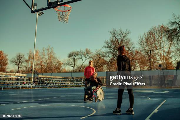 young disabled man in wheelchair playing basketball with his sisters - basket sport stock pictures, royalty-free photos & images