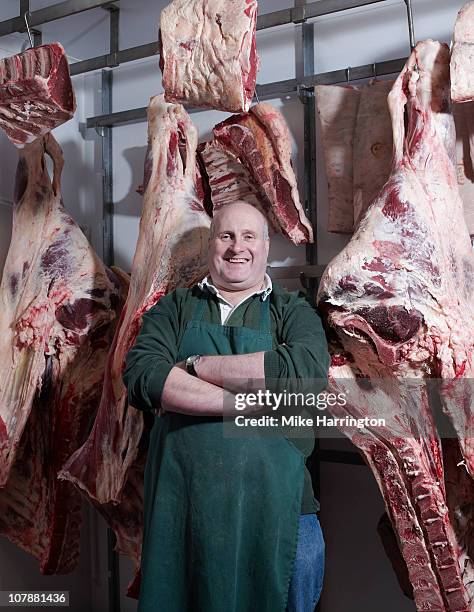 traditional butcher standing by chilled meat - butcher foto e immagini stock