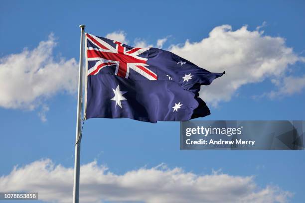 australian flag flying in the wind with blue sky and clouds - australische flagge stock-fotos und bilder