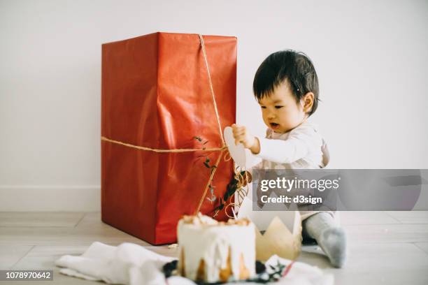 cute baby girl sitting behind a cake and unwrapping a large box of christmas present in christmas party - happy birthday crown stock pictures, royalty-free photos & images