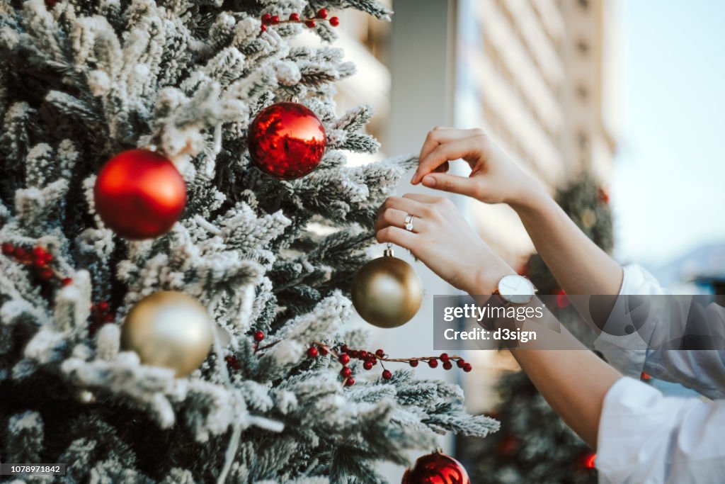 Cropped hand of woman decorating and hanging baubles on Christmas tree