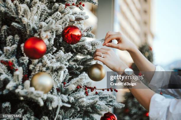 cropped hand of woman decorating and hanging baubles on christmas tree - decoration foto e immagini stock