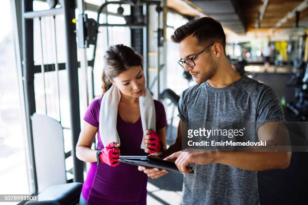 vrouw en persoonlijke trainer maken oefening plan in sportschool - sport tablet stockfoto's en -beelden