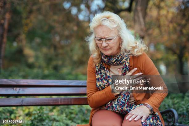 elderly woman having chest pains or heart attack in the park - women pain stock pictures, royalty-free photos & images