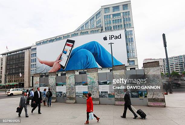 People walk past and look at a section of the Berlin Wall in front of a giant billboard featuring Apple's new iPad on June 15, 2010 at Potsdamer...