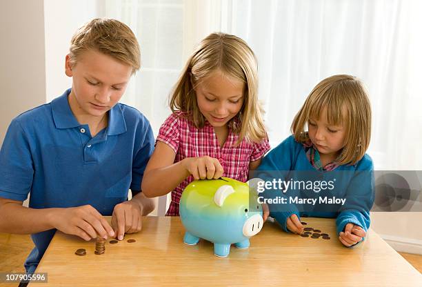 three young siblings with a piggy bank. - blonde girl piggy bank stock-fotos und bilder