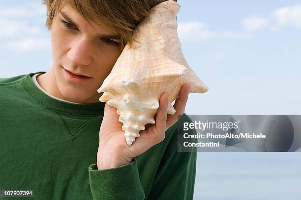 young male listening to conch shell - conch shell stockfoto's en -beelden