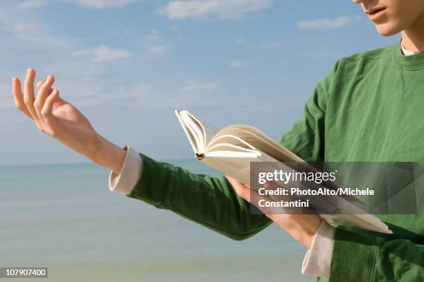 young male reading aloud from book at the beach - poetry stock pictures, royalty-free photos & images