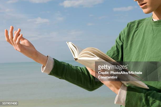 young male reading aloud from book at the beach - poetry literature imagens e fotografias de stock