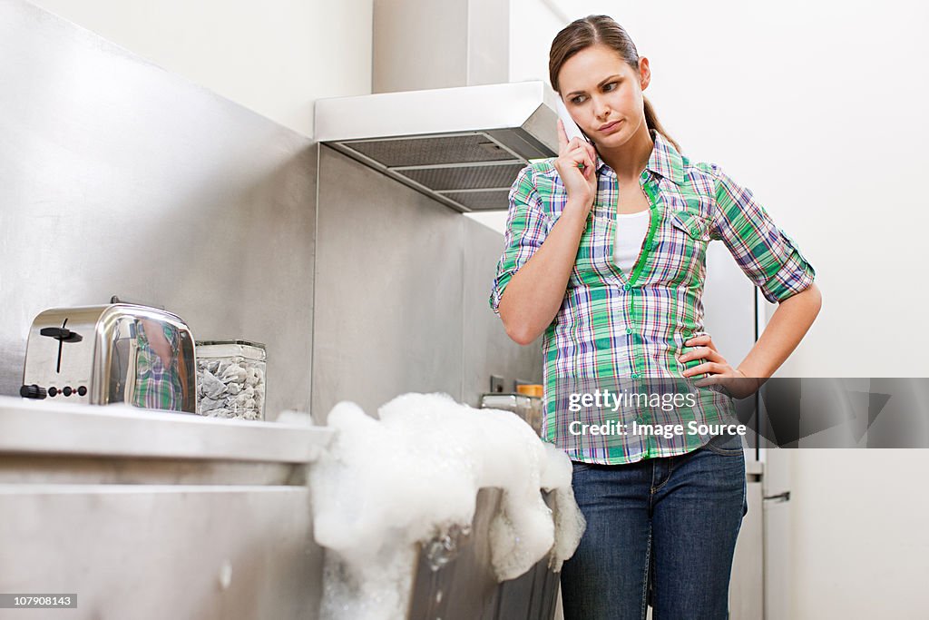 Young woman on phone with overflowing dishwasher