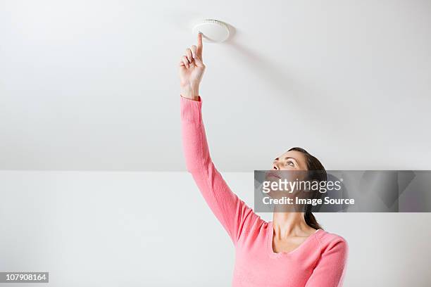 young woman testing smoke alarm on ceiling - sirene stockfoto's en -beelden