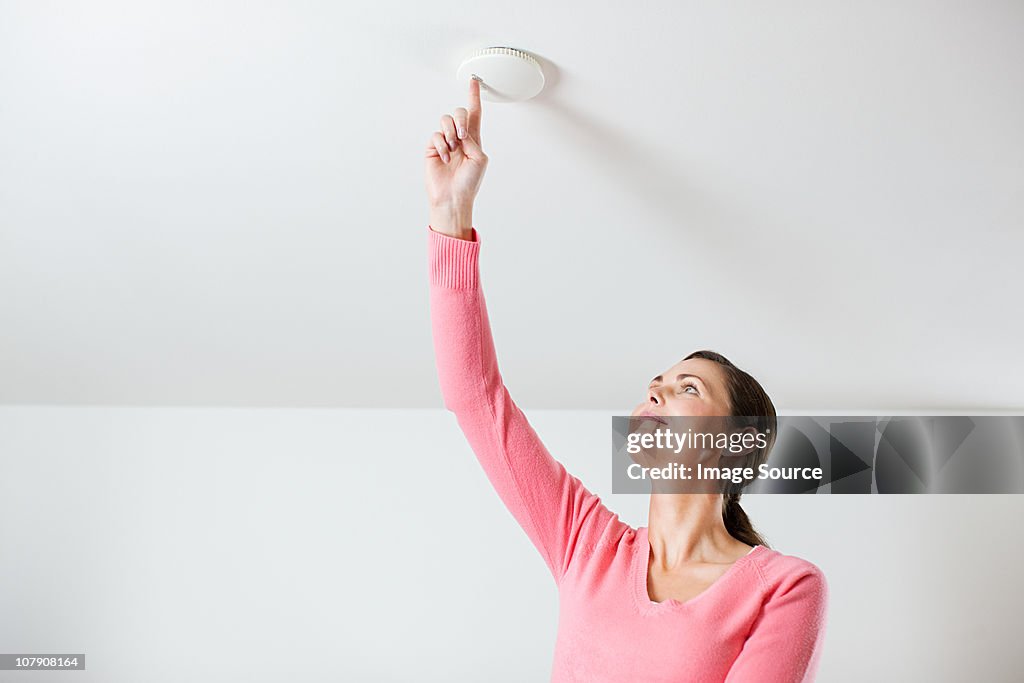 Young woman testing smoke alarm on ceiling