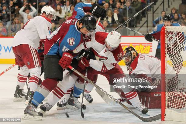 Brandon Yip of the Colorado Avalanche tries to collect the puck in the crease as Eric Belanger of the Phoenix Coyotes defends and goalie Jason...