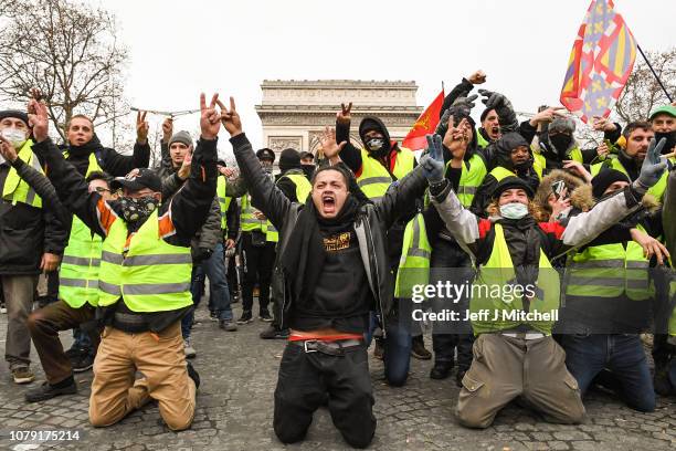 Demonstrators kneel and gesture with victory signs as they take part in the demonstration of the yellow vests near the Arc de Triomphe on December 8,...