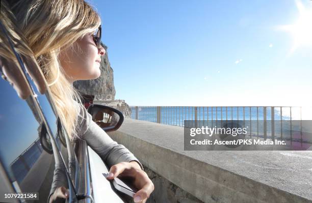 young woman relaxes in car seat, looks out to sea - liguria stock photos et images de collection