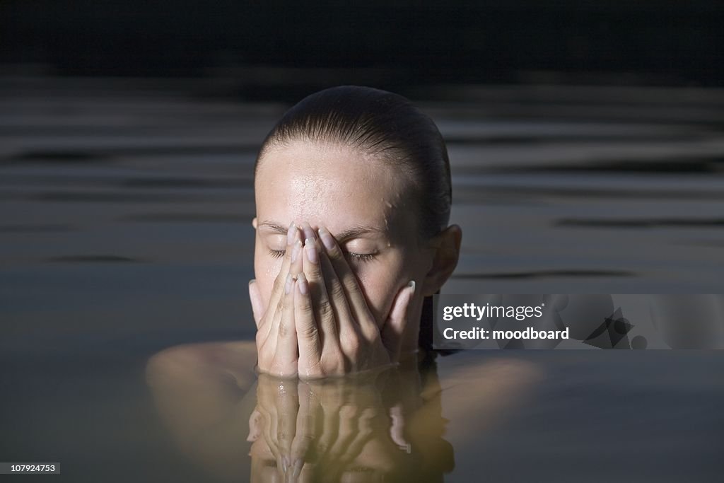 Young woman covers her face with her hands in water