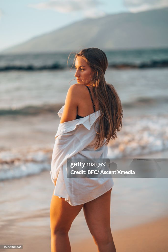 Young woman stands on beach, looks out to sea