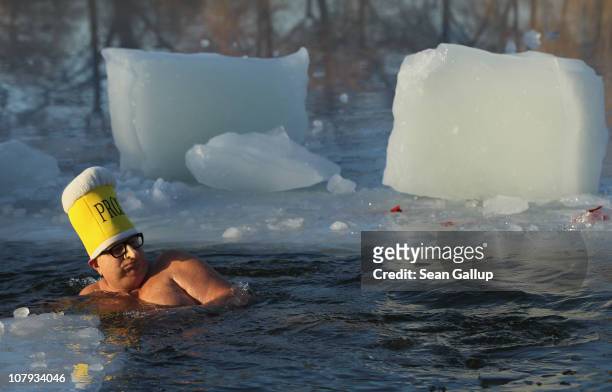 An ice swimming enthusiast wearing a hat in the shape of a beer mug and a fake, elongated nose takes to the frigid waters of Orankesee lake during...
