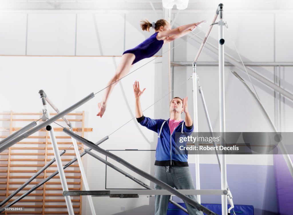 Trainer guiding young gymnast on parallel bars