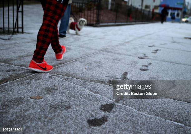 Pedestrian passes through a light dusting of snow on a Columbia Road sidewalk in the Dorchester neighborhood of Boston on Jan. 8, 2019.