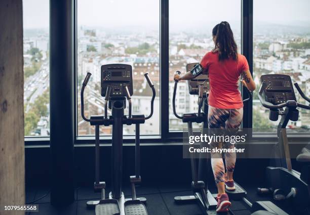 rückansicht einer frau auf einem cross-trainer in einem fitnessstudio trainieren. - cross trainer stock-fotos und bilder